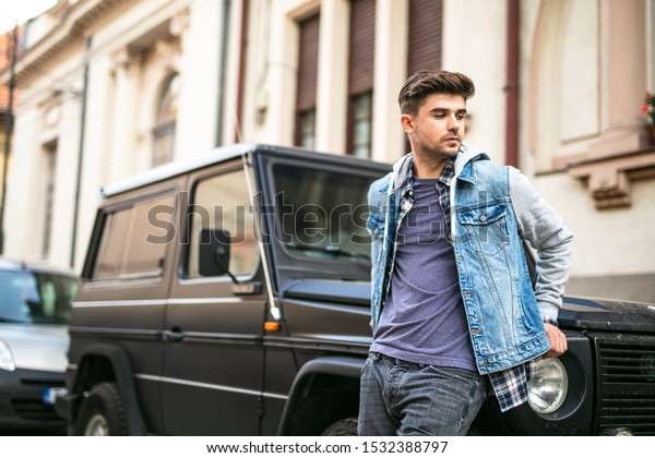frontal pose with a cool\
young man standig in front of his cool muscle black car looking\
confident