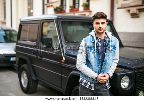 frontal pose with a cool
young man standig in front of his cool muscle black car looking
confident