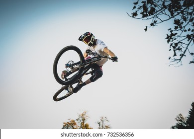 Frontal Shot Of A Mountain Biker Jumping Over A Dirt Jump In A Bike Park Performing A Tail Whip .