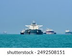 Frontal view of 2 large ships getting their bunkering done with the bunker vessels alongside and some other vessels in the background at the anchorage.