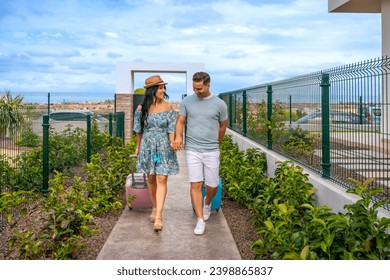 Frontal view of a couple holding hands carrying luggage while arriving at an hotel - Powered by Shutterstock