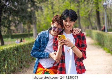 Frontal view of a multiracial young gay couple using phone in a park - Powered by Shutterstock