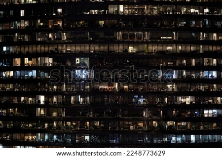 Frontal view of night facade of building with a lot of windows with light. life in every window. night view of the glass facade of an office skyscraper.