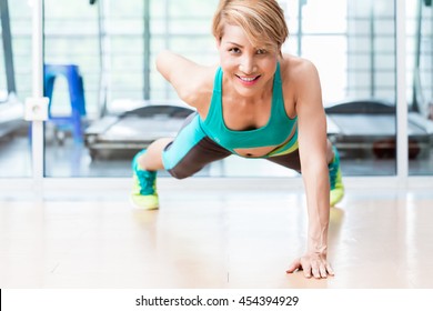 Frontal View Of Smiling Young Woman Doing One Arm Pushup In Gym