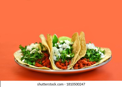 Frontal view of three delicious tacos with vegan meat and coriander, in orange background.