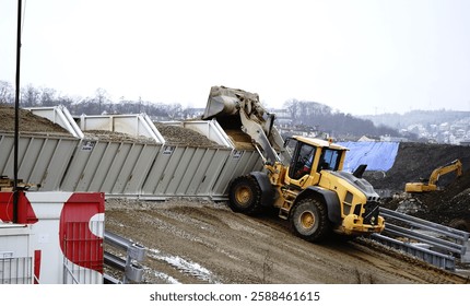 A front-end loader with a bucket scoop loading sand into containers. The machine efficiently lifts and transfers the sand, preparing it for transport with precision and power.