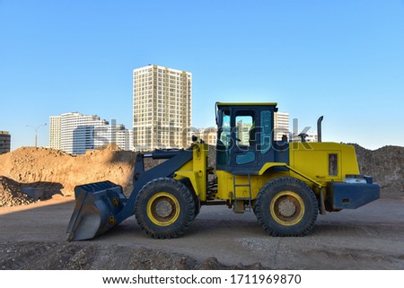 Front-end loader working at construction site. Earth-moving heavy equipment for road work. Public works, civil engineering, road building. Construction machinery for loading, lifting cargo