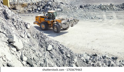 Front-end loader works in a quarry against the backdrop of limestone debris, close-up, panorama.