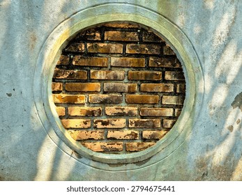 A front-facing shot of a unique architectural element featuring a circular concrete window frame filled with aged, weathered red bricks