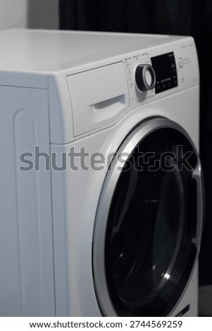 Front-loading washing machine with a digital control panel and glass door, set against a dark curtain backdrop in a contemporary laundry area