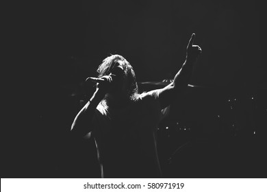 Frontman silhouette singing to the microphone to the crowd on a concert in a stage backlights. Black and white.