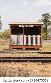 A front-view, centered shot of the small, rustic Petford railway station building in rural Australia. The simple orange-painted structure features a corrugated metal roof, a white picket fence gate, and a prominent 