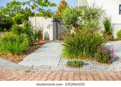 The frontyard of a modern house, garden details with colorful plants, dry grass beds surrounded by grey rocks. - Shutterstock ID 2352064235