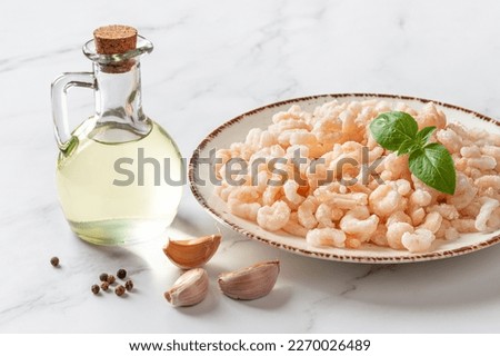 Frosen shrimps on a plate over marble countertop. Cooked peeled prawn tails, olive oil and garlic prepared for cooking. Sea crustacean for low calorie healthy meals. Seafood recipe. Front view.