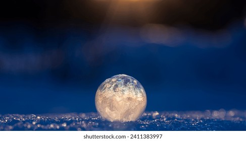 frosen soap bubble on top of snow, setting sun in the background ,winter time