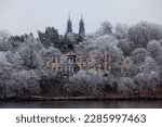 Frost covered trees in front of old building on prison island Långholmen in Stockholm, Sweden. The towers on the church Högalidskyrkan in the background.