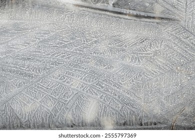 The frost creates delicate, lace-like patterns on the surface of the puddle, showcasing the artistry of nature.
