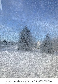 Frost on a window with pine trees behind 