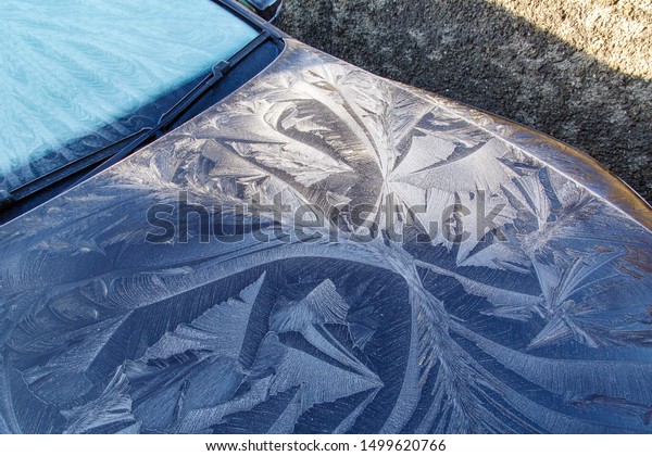 Frost patterns on a car hood\
with black paint work - winter hoar frost creating unusual\
shapes.