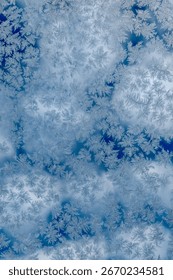 Frost patterns on a window forming natural ice crystals, creating an abstract winter texture with sky reflections.