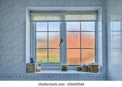 Frosted glass bathroom window with distorted orange/blue exterior, and various items on the windowsill.