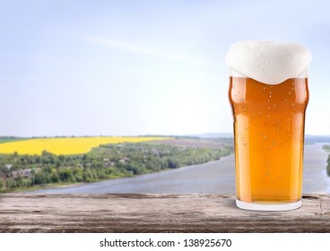 Frosty glass of light beer on a wooden table with summer scene background