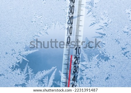 Frosty winter window with ice patterns and a thermometer showing a minus temperature.