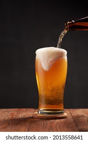 Frothy and amber brilliance craft beer, pouring in the glass from the bottle on a wooden bar.  Dark background. Shallow depth of field photo with copyspace. - Shutterstock ID 2013558641