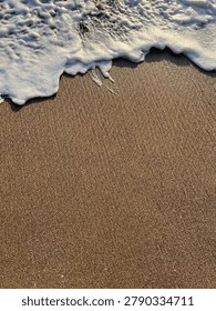 Frothy sea waves gently rolling onto soft sand, showcasing dynamic textures and refreshing coastal atmosphere.