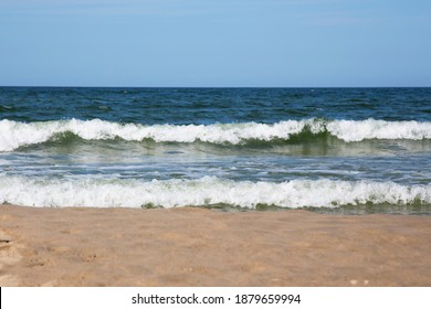 frothy white waves on the sandy beach of the Baltic Sea. Blue sea and bright blue sky, high tide