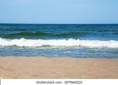 frothy white waves on the sandy beach of the Baltic Sea. Blue sea and bright blue sky, high tide
