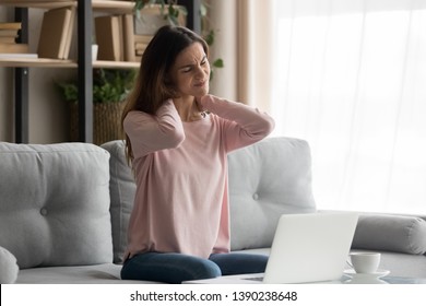 Frown Woman Sitting On Couch Near Computer Take Break Touches Her Neck Suffers From Painful Feelings Ache Caused By Poor Wrong Posture, Sedentary Work, Sitting At Laptop For Long Period Concept Image