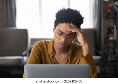 Frowning African Woman Sit At Desk With Laptop Touch Forehead Feels Unwell Looks Tired, Feeling Badly, Experiences Information Overload Having Long Hard Workday. Stress At Work, Headache, Tech Concept