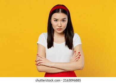 Frowning Angry Gloomy Sad Young Woman Of Asian Ethnicity She 20s Years Old Wears White T-shirt Hold Hands Crossed Isolated On Plain Yellow Background Studio Portrait. People Emotions Lifestyle Concept