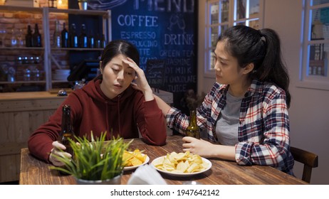 frowning asian chinese girl comforting sad best friend and touching her shoulder while drinking beer at night club. - Powered by Shutterstock