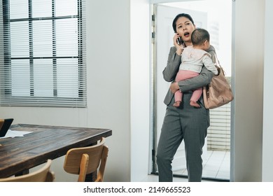 Frowning Asian Woman Ceo Entering House Holding Infant Is Calling Her Colleague Handling Trouble At Work. Busy Female Manager Arriving Home With Kid Is Nagging At Worker Through Phone For Mistakes.