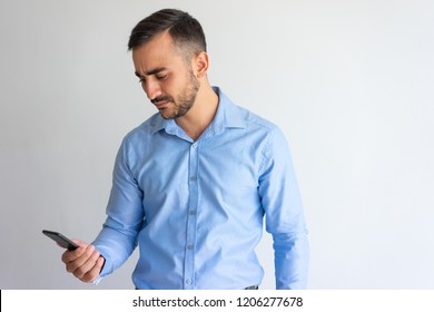 Frowning Concerned Businessman Focused On Phone Screen. Puzzled Young Man Using Smartphone. Communication Or Bad News Concept