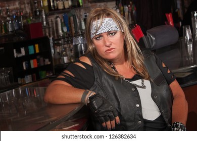 Frowning female motorcycle gang member sitting in bar