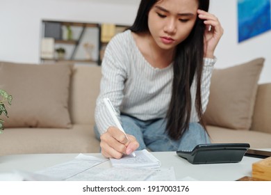 Frowning Pretty Young Asian Woman Counting Sum Of Monthly Expenses And Utility Bills And Taking Notes In Notebook