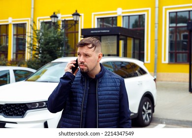 Frowning Tense Sullen Or Sad Concentrated Young Caucasian 34 Years Old Man With Goatee Beard Talks On Smartphone On Street Near White Car. Waist Up Lifestyle Business Portrait, Difficult Conversation