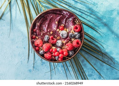 Frozen acai smoothie in coconut shell with raspberries, banana, blueberries,  fruit and granola on concrete background. Breakfast, healthy meal for summer vibes, top view, space for text - Shutterstock ID 2160268949