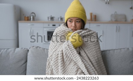 Frozen Asian Chinese Korean woman sick sad girl freezing sit in cold apartment suffer low temperature froze freeze covered in warm blanket hat and mittens winter season heating problem in home kitchen