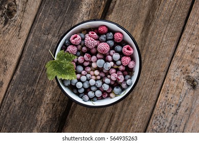 frozen berries, black currant, red currant, raspberry, blueberry in enamelled bowl decorated by currant leaf on wooden table in rustic style,  top view.