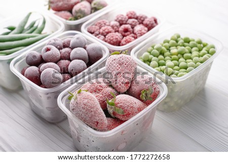Frozen berries and vegetables in plastic boxes on a light background.