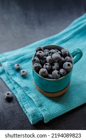 Frozen Blueberries In A Blue Mug On A Folded Blue Napkin On The Table, Vertical Orientation, Top View