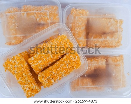 Frozen breaded snacks in plastic containers, ready to fry. Indonesian-style food coated in orange bread crumbs, neatly packed.