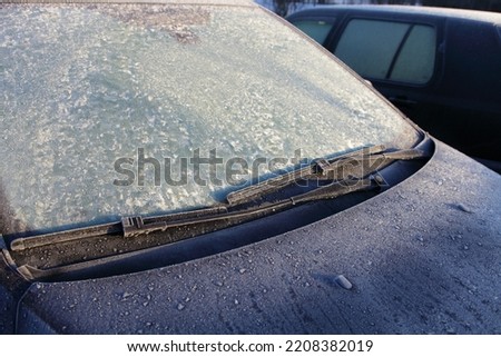 Frozen Car windscreen with wiper blade and hood on frosted windshield glass. Autumn morning frosts