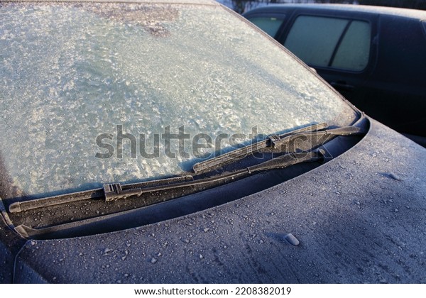 Frozen Car windscreen with\
wiper blade and hood on frosted windshield glass. Autumn morning\
frosts