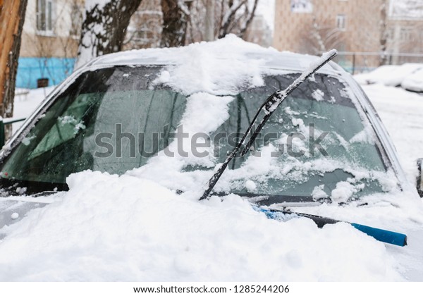 Frozen\
car windshield covered with snow on a winter day. A windscreen\
wiper or windshield wiper is a device used to remove rain, snow,\
ice and debris from a windscreen or windshield\
