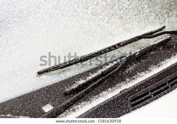 Frozen car wipers. Dangerous ice on the road.\
Frost on the windshield of the car. Detail of a frozen car window.\
Danger in transport.
